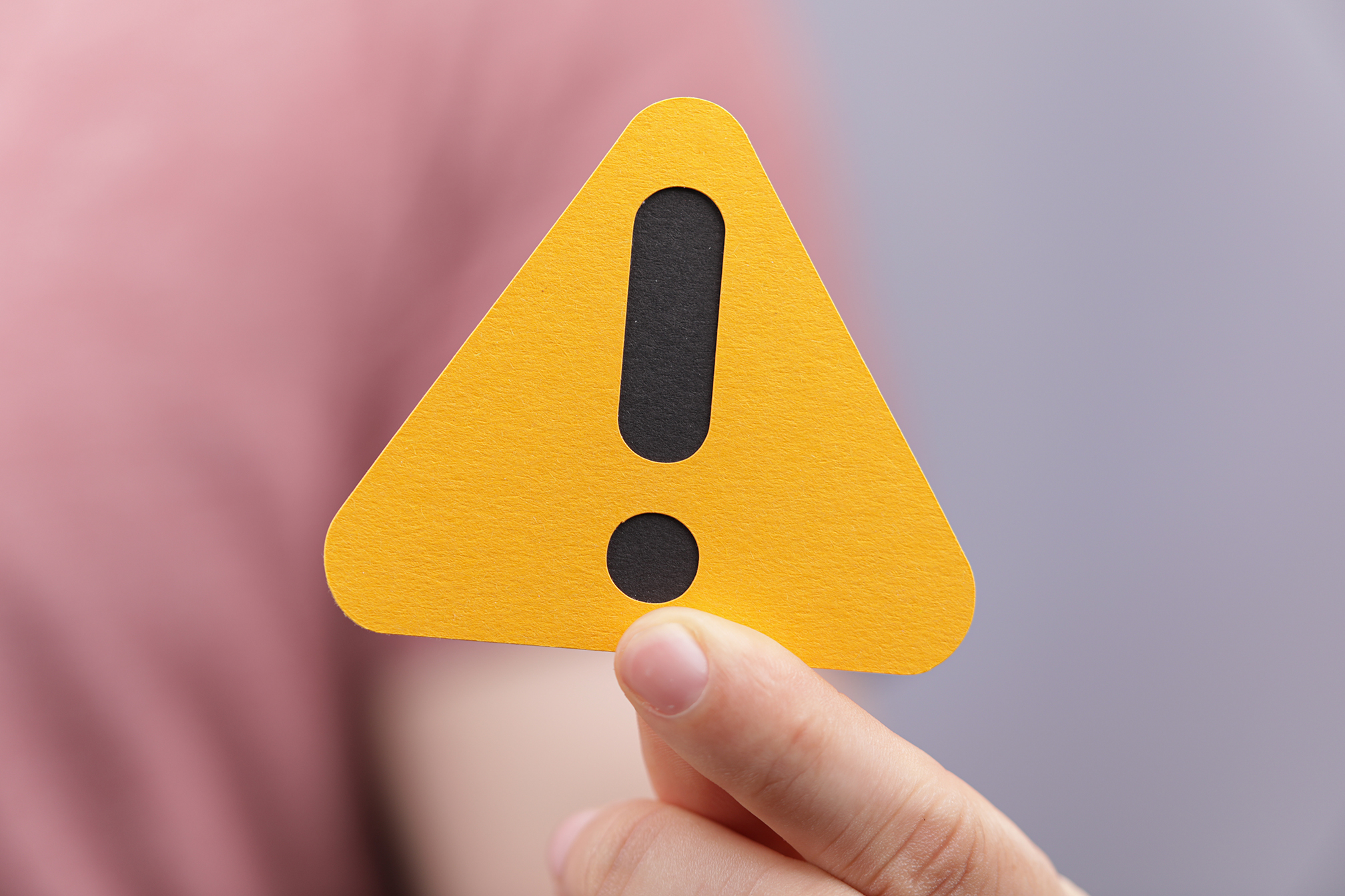 A sign of the exclamation mark on a yellow paper in the hands of a man